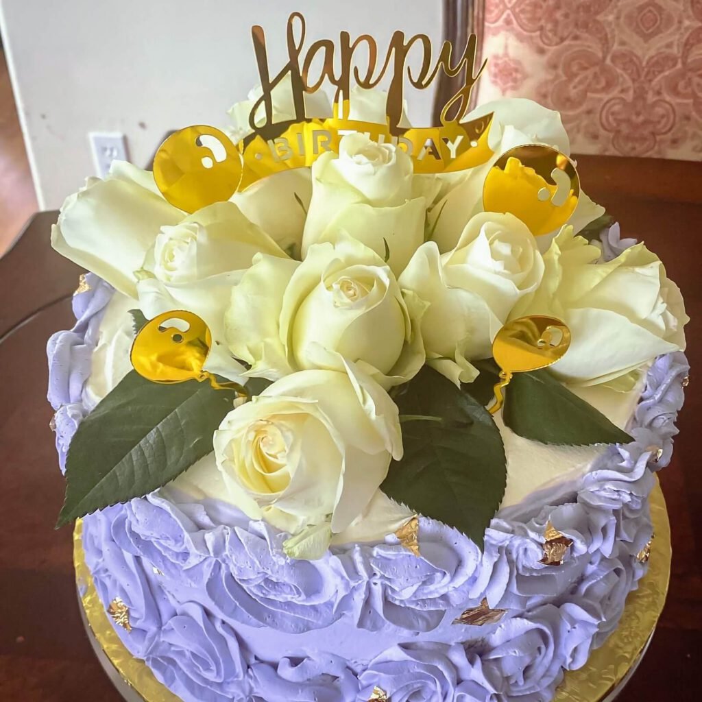 a happy birthday cake with beautiful white roses, happy birthday sign, and elaborate cake decoration on the side