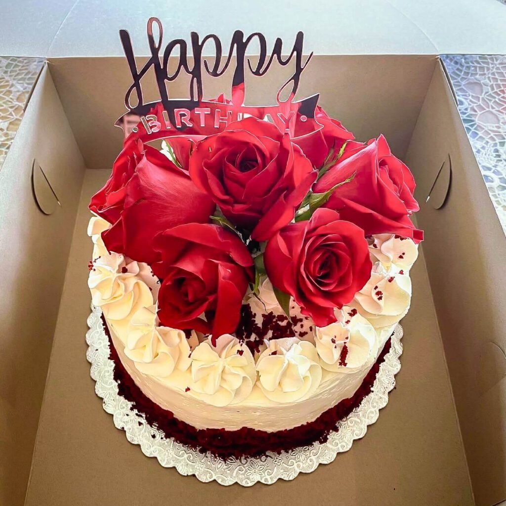A beautiful vanilla cake with chocolate at the bottom, with red roses and a happy birthday sign.