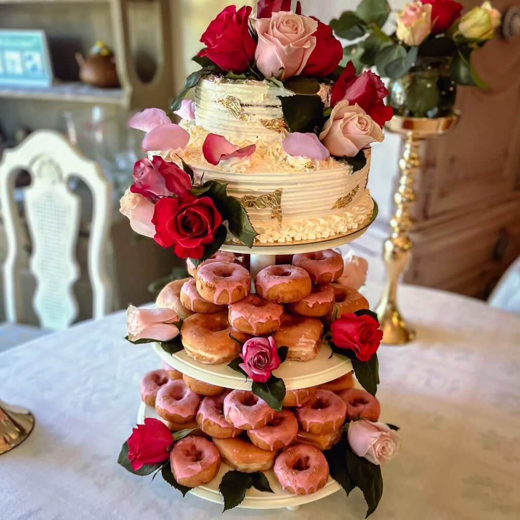 A beautiful vanilla cake decorated with red and pink roses, layered with donuts underneath.