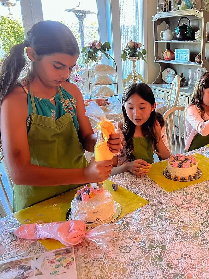 One girl decorating a cake while another girl looks at the work in progress.