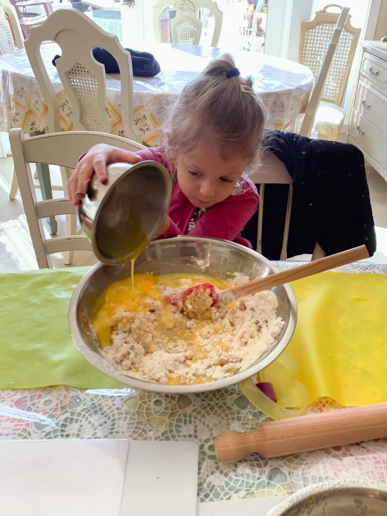 A little girl mixes her egg onto the dough to start mixing it up.