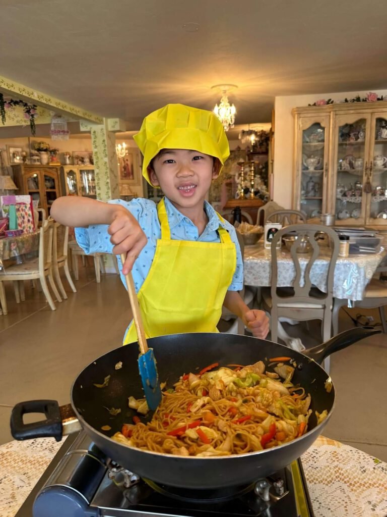 A boy dressed with a yellow apron and a yellow hat cooks delicious pasta.